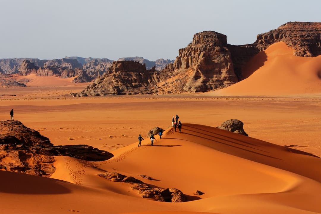 Paysage désertique de Djanet mêlant dunes dorées, roches du Tassili et silhouettes de visiteurs.